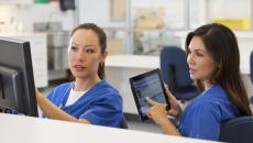 Healthcare worker with tablet looking at screen another worker is pointing at