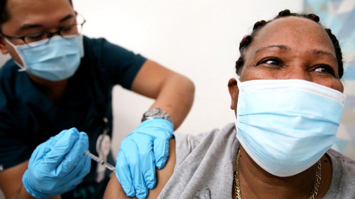 A person gets vaccinated by another person, both in masks